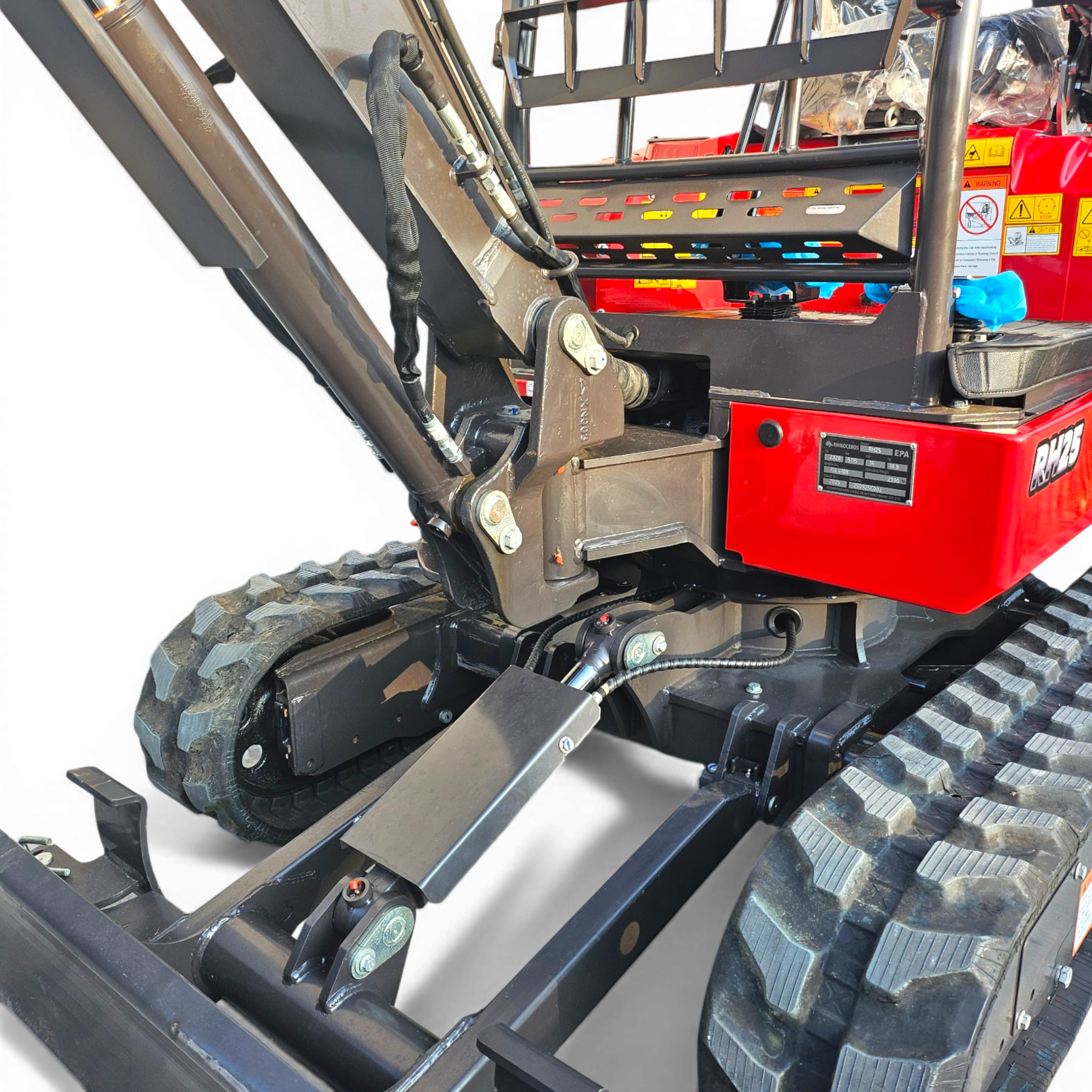Close-up of a heavy equipment boom with hydraulic hoses, metal frame, and track treads; red body with warning labels visible in the background.