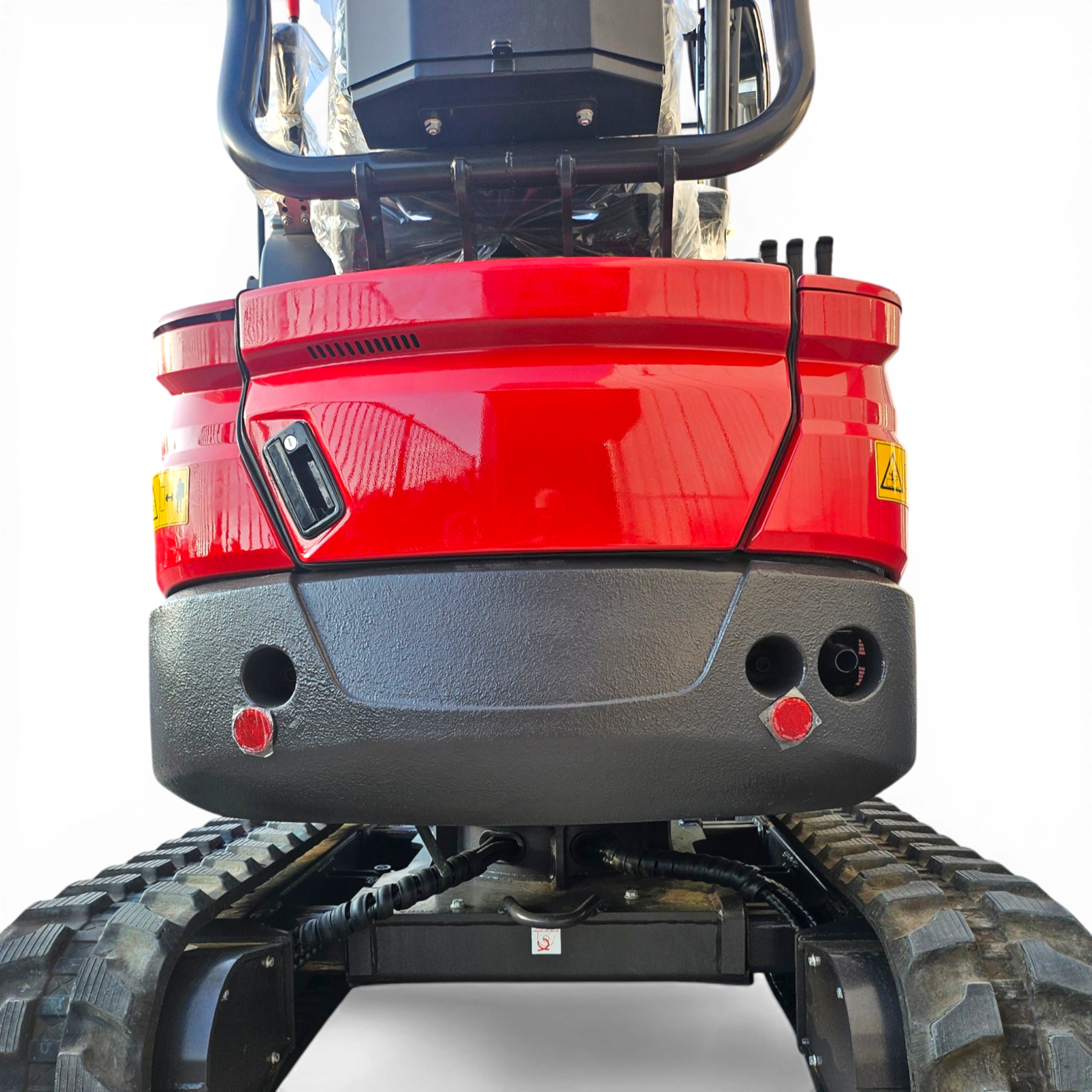 Rear view of a red heavy machinery cab with exposed hydraulic hoses and large rugged tires beneath it.