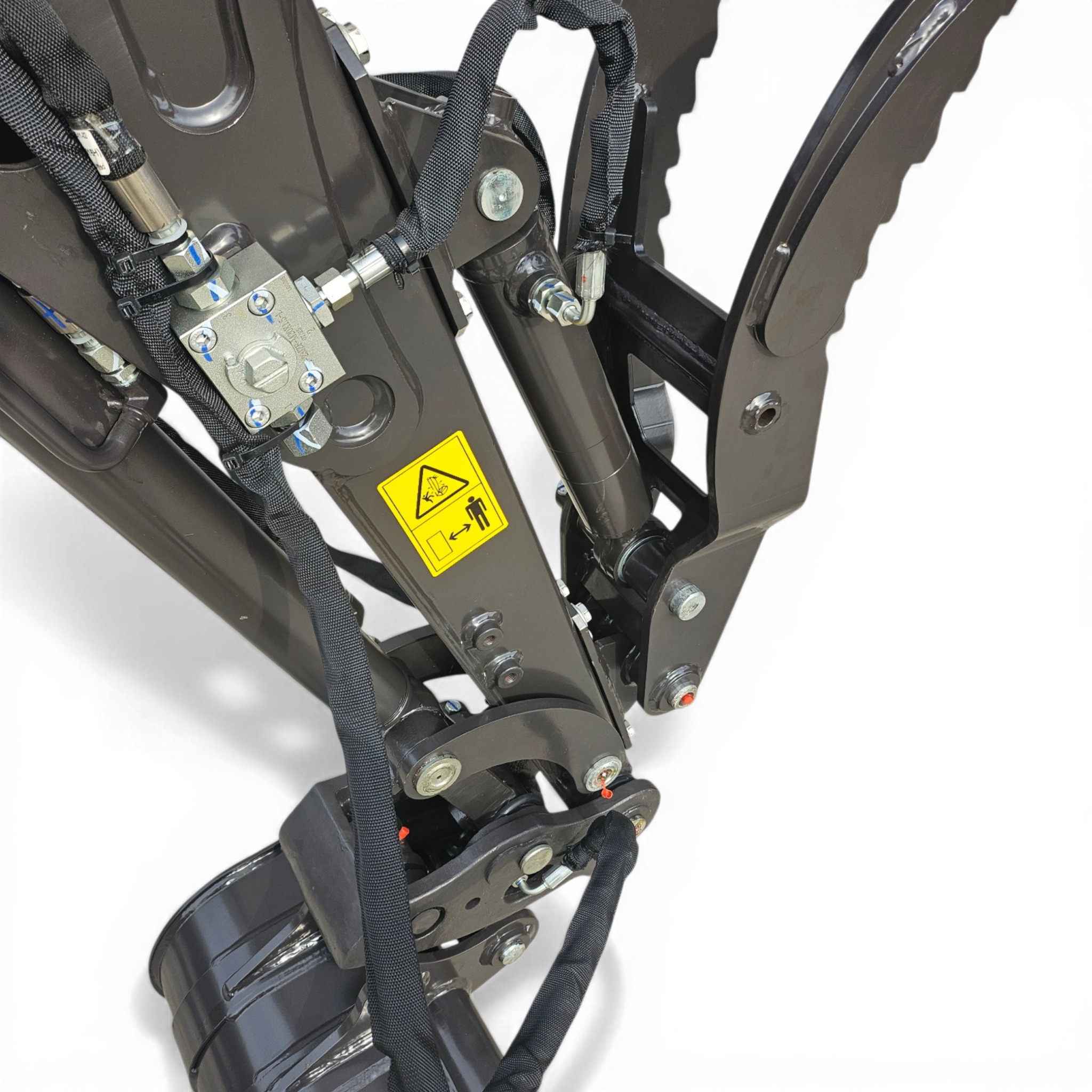 Close-up of a hydraulic/mechanical assembly with braided hoses, metal fittings, and bolts on a dark frame, including a yellow warning label.