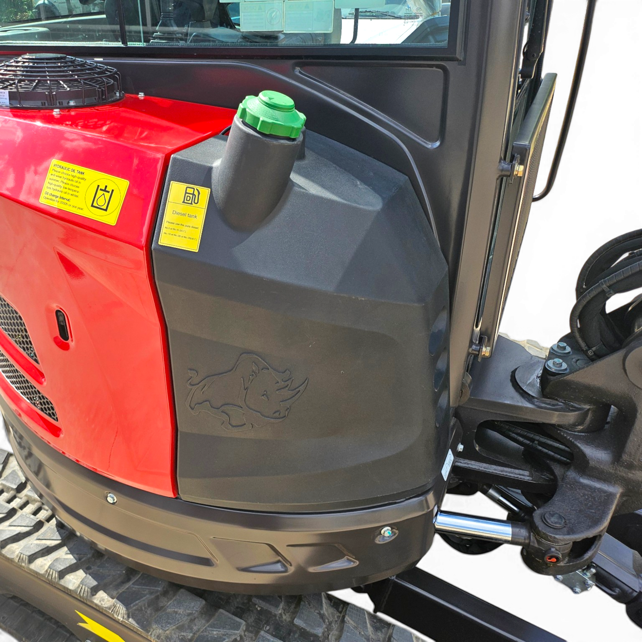 Close-up of the front left engine area on a red and black truck, showing a green fuel cap and yellow warning labels near the hood edge.