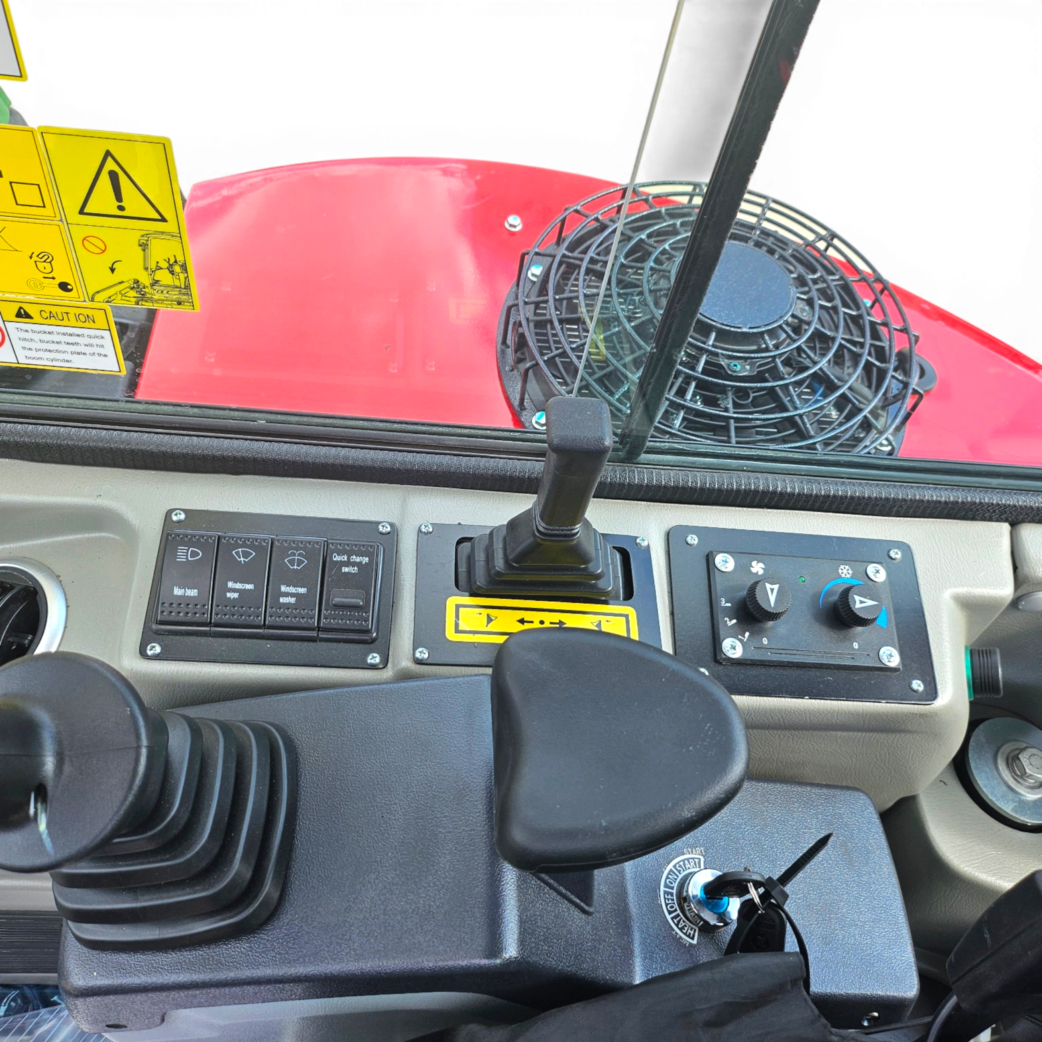 Close-up of a tractor dashboard with a joystick, control switches, and a fan grille visible on the right; yellow warning decals are on the left edge.