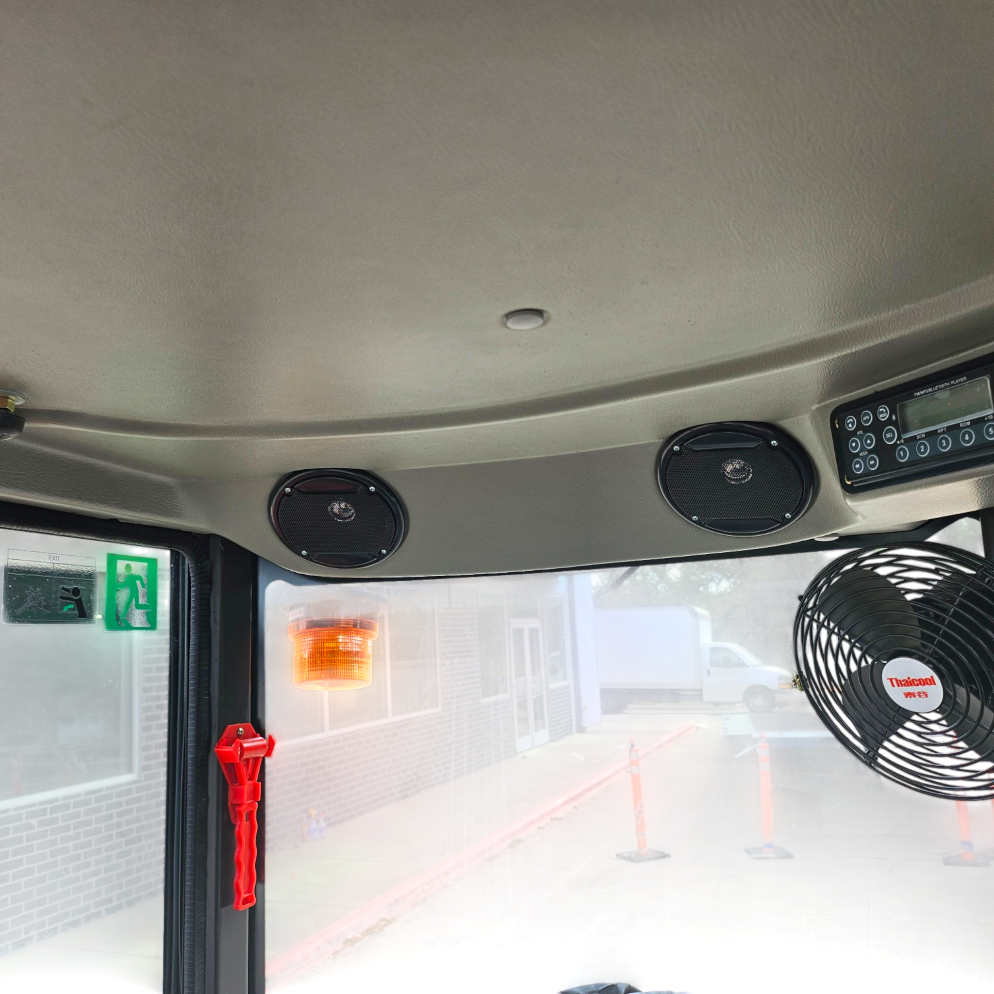 Interior of a vehicle cab showing ceiling, speakers, and a central dome light with an orange warning beacon outside the window; exterior scene includes construction cones and a sign.