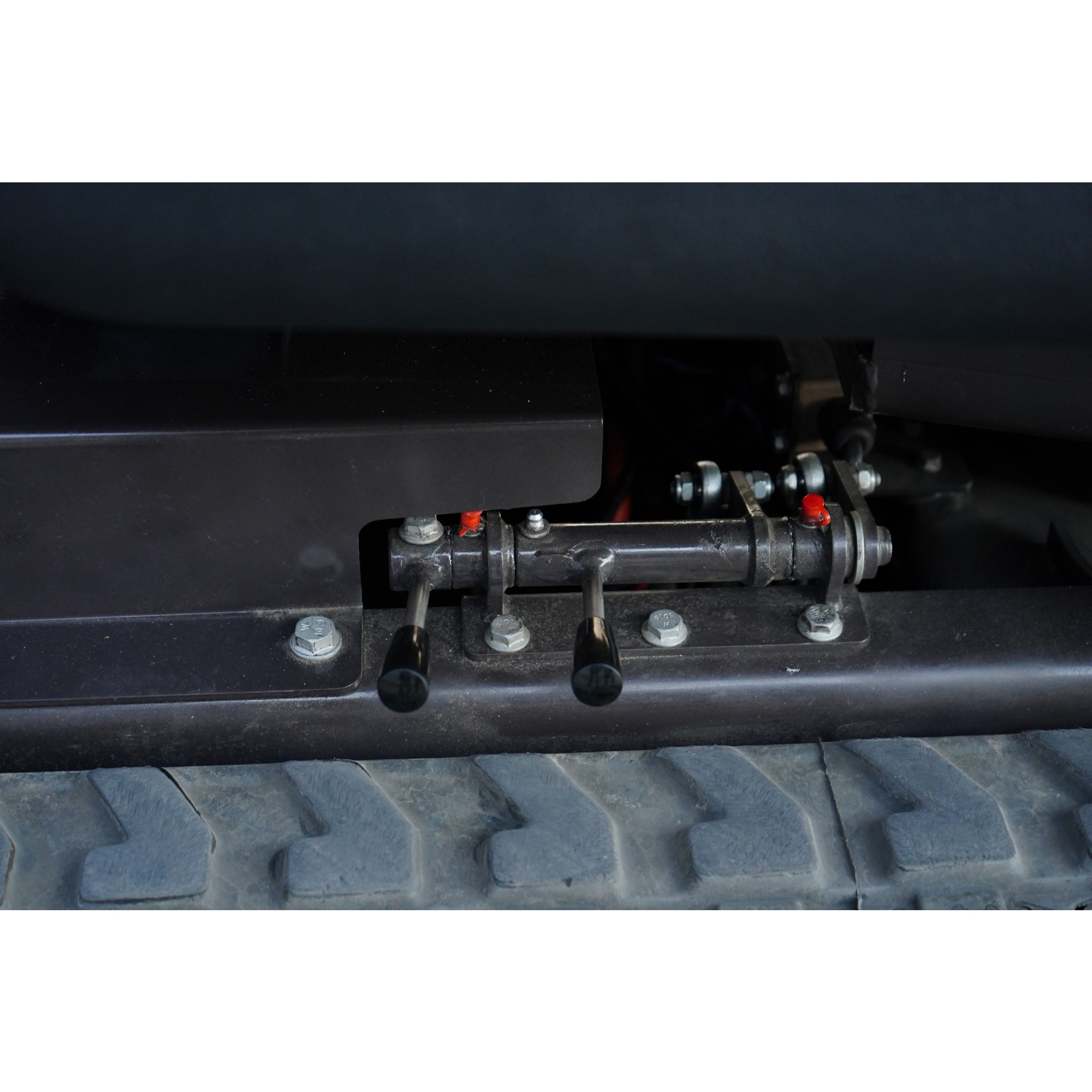 Close-up of a dark metal surface with bolts, nuts, and hydraulic tubes in an industrial undercarriage area.