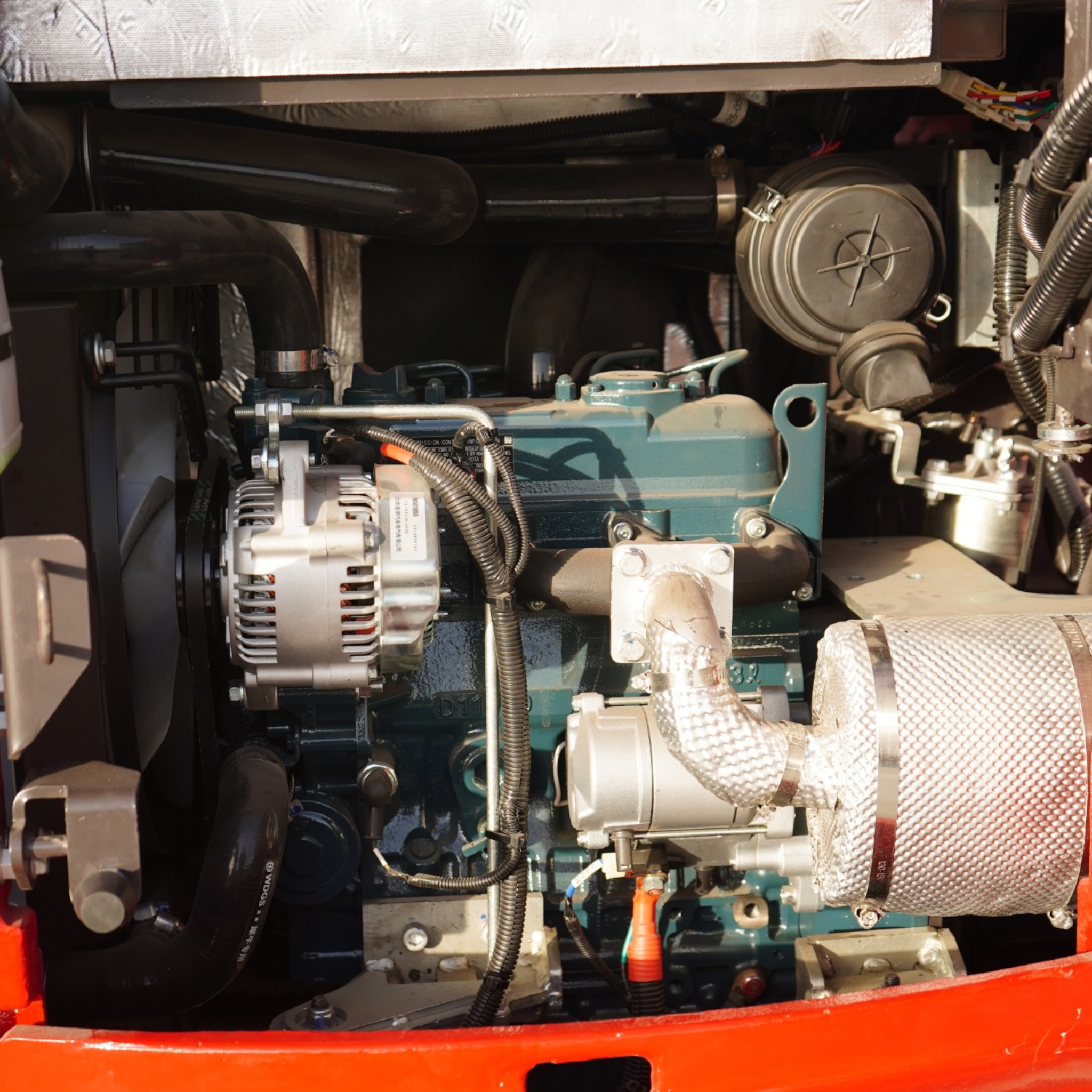 Close-up of a diesel engine bay with black pipes, braided hoses, and wiring inside a red/orange chassis frame.