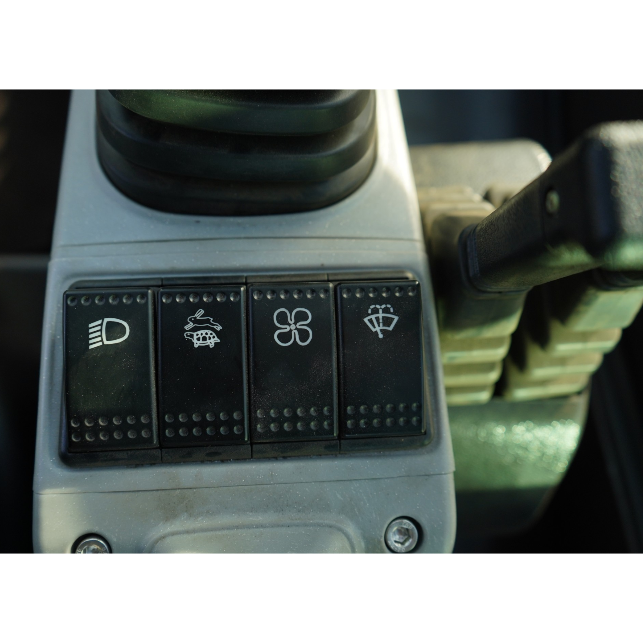 Close-up of a car's dashboard buttons showing a headlight icon, turtle and rabbit cruise control icons, and a windshield-wiper symbol on the far right.
