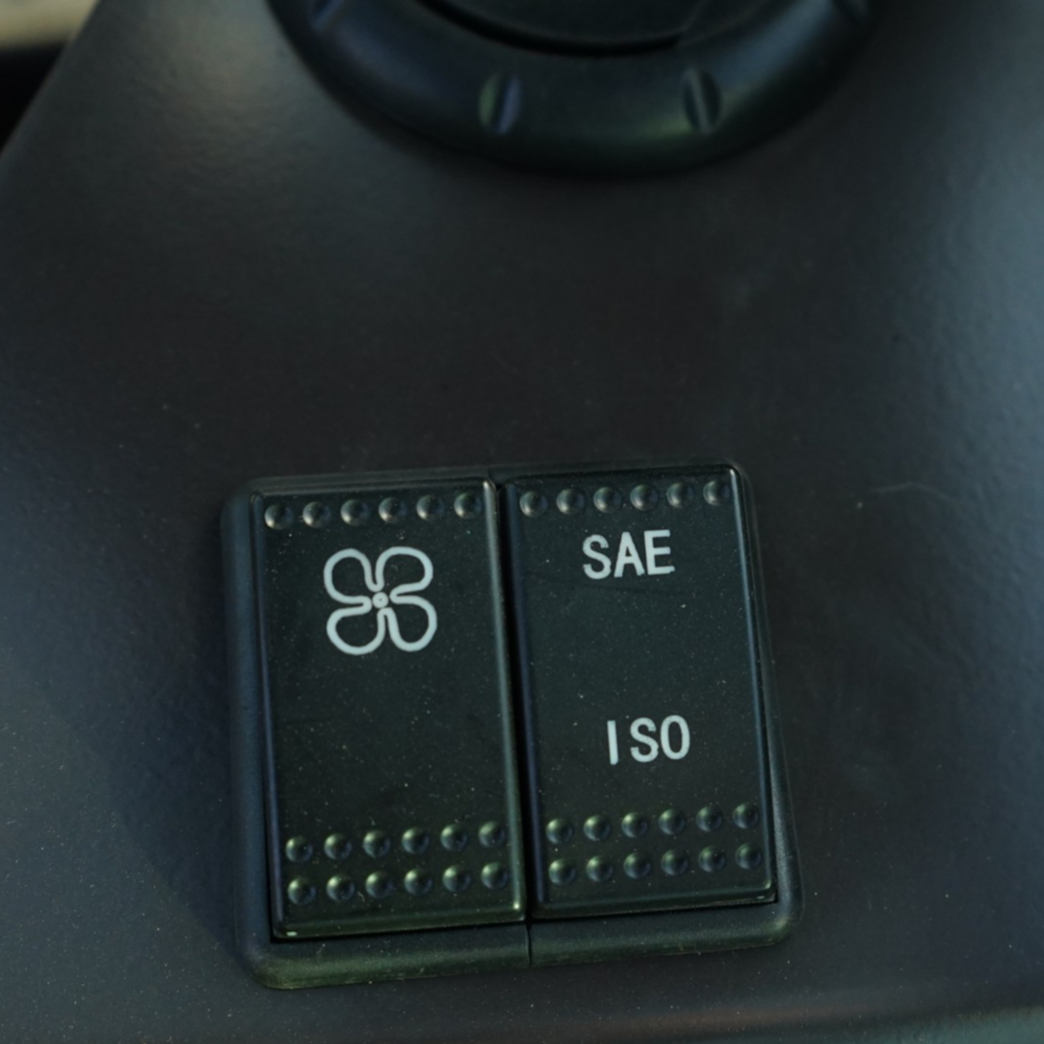 Close-up of two black electrical connectors with rows of metal pins, labeled SAE and ISO on a dark surface.