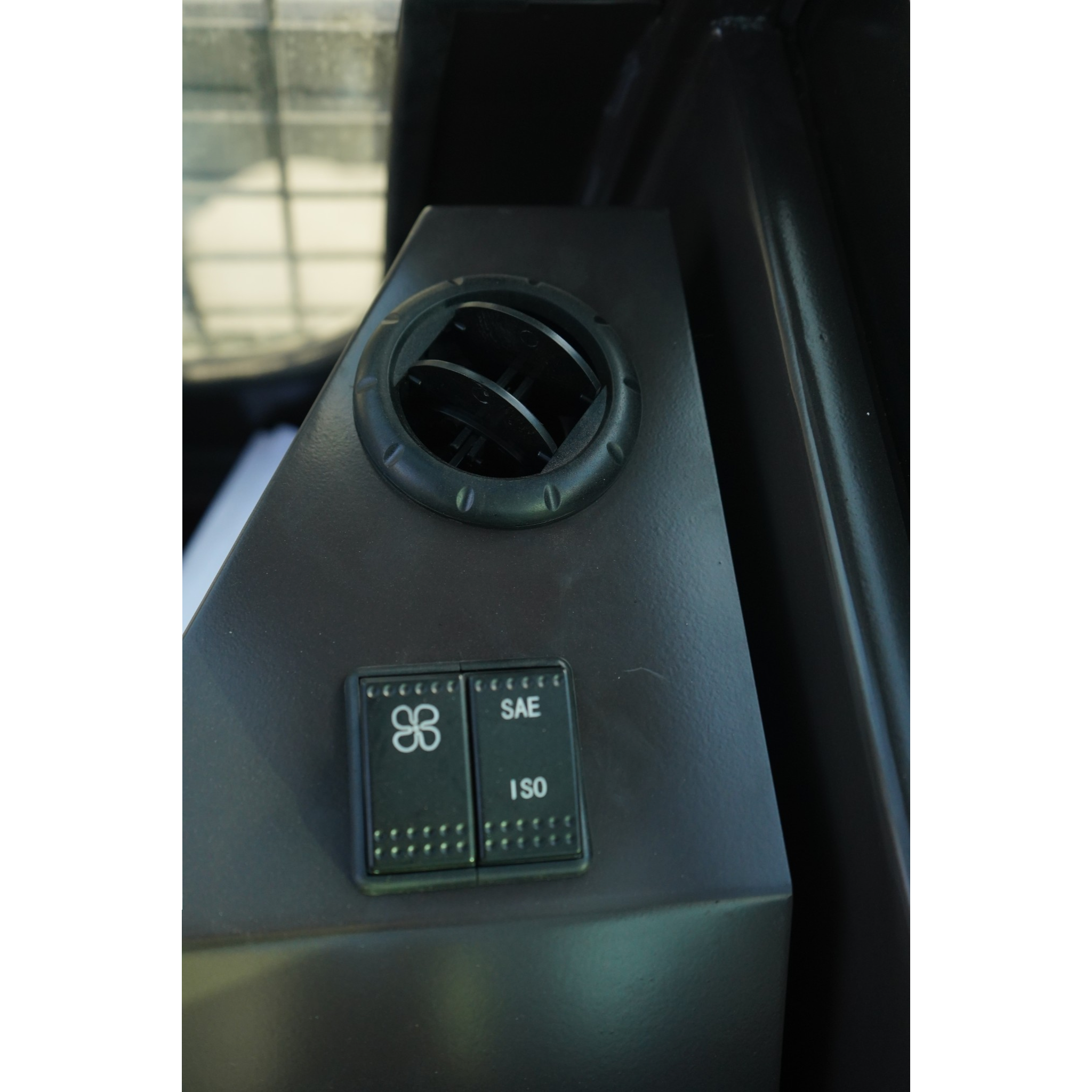Close-up of a circular car vent on a dark dashboard with a small ISO/SAE switch beneath it.