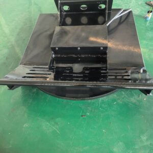 Black-painted metal industrial component with a sloped top plate and perforated base resting on a green workshop floor.