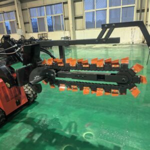 Industrial machine with a tracked base and long black arm featuring orange tines, in a factory setting with green floor and large windows.