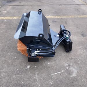 Close-up of a black metal street-sweeper attachment with orange bristles mounted on a machine, outdoors on asphalt parking lot edge.
