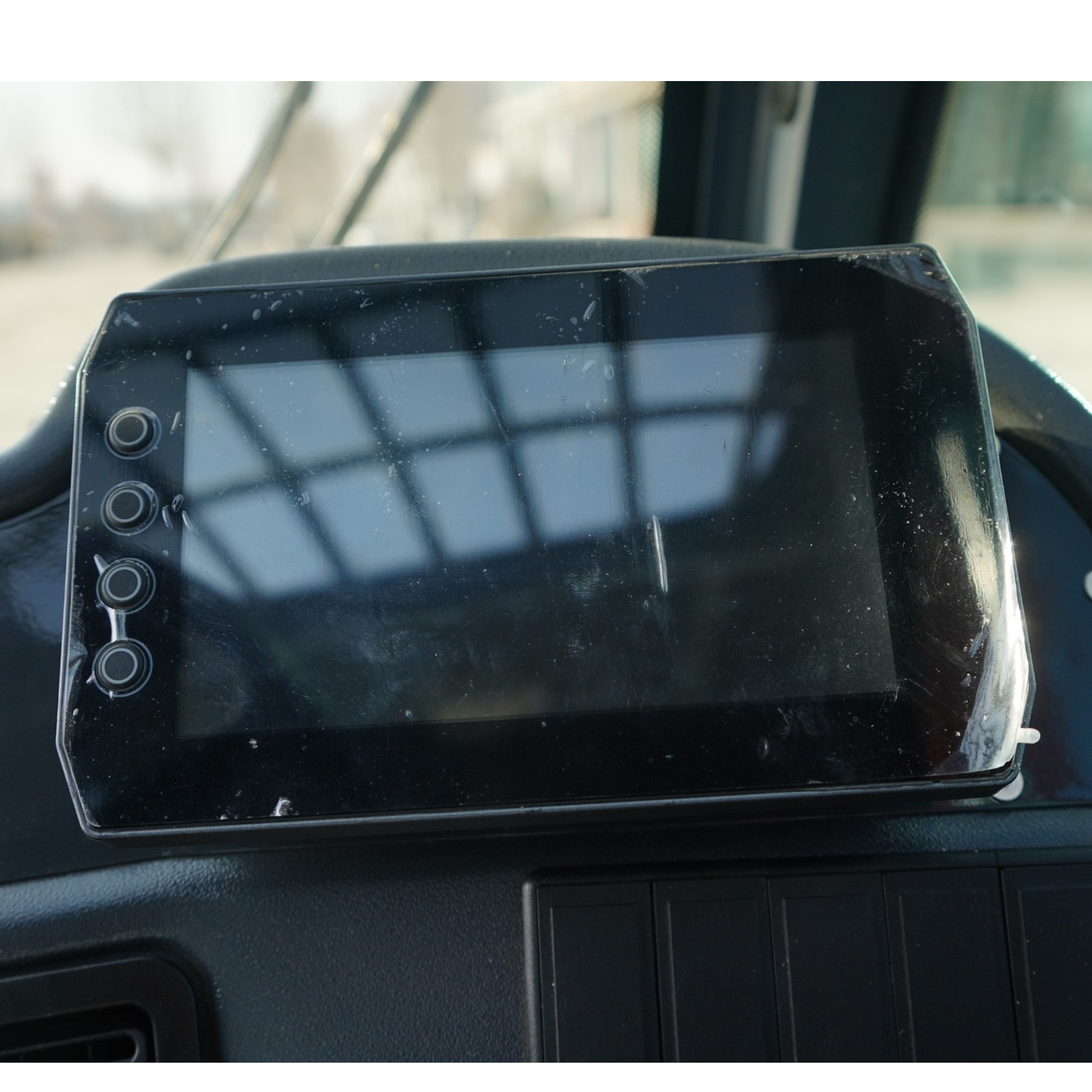 Close-up of a dusty car dashboard tablet mounted on the dash with a blurred windshield in the background.