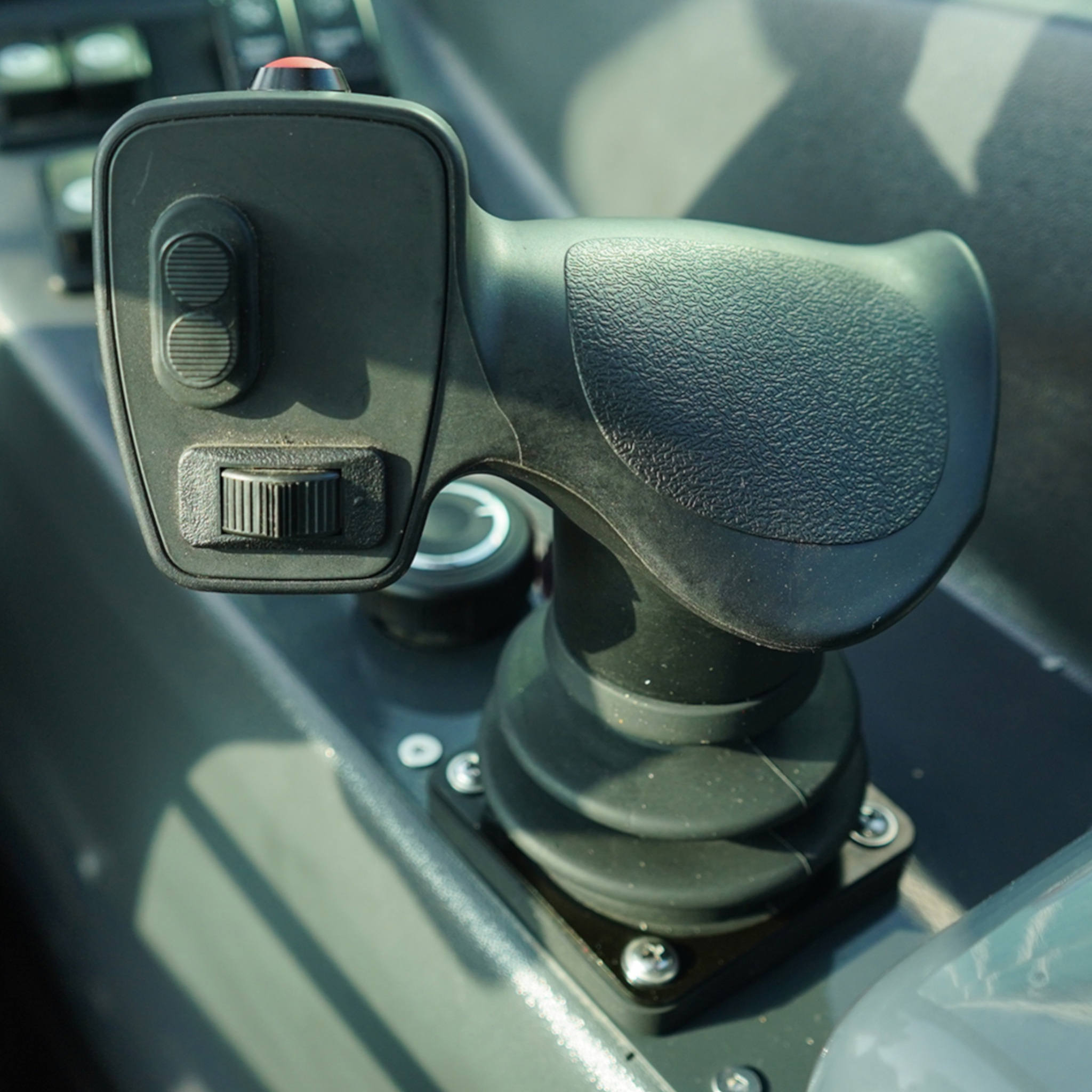 Close-up of a car's steering column with a textured grip, a red push button, and two circular rocker controls on a nearby panel.