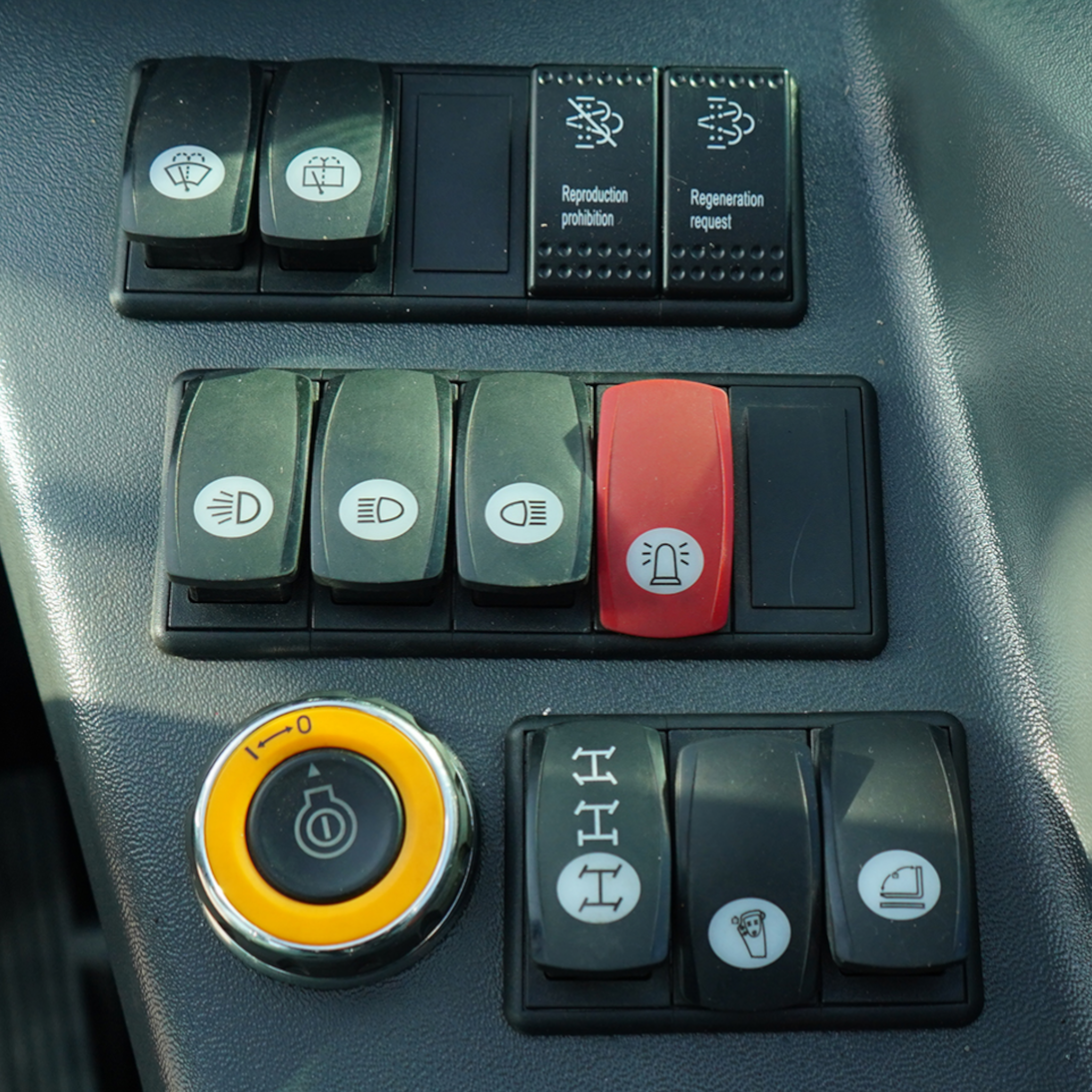 Car dashboard switch panel with windshield wiper controls, a yellow circular ignition dial, and two labeled buttons reading 'Reproduction prohibition' and 'Regeneration request'.