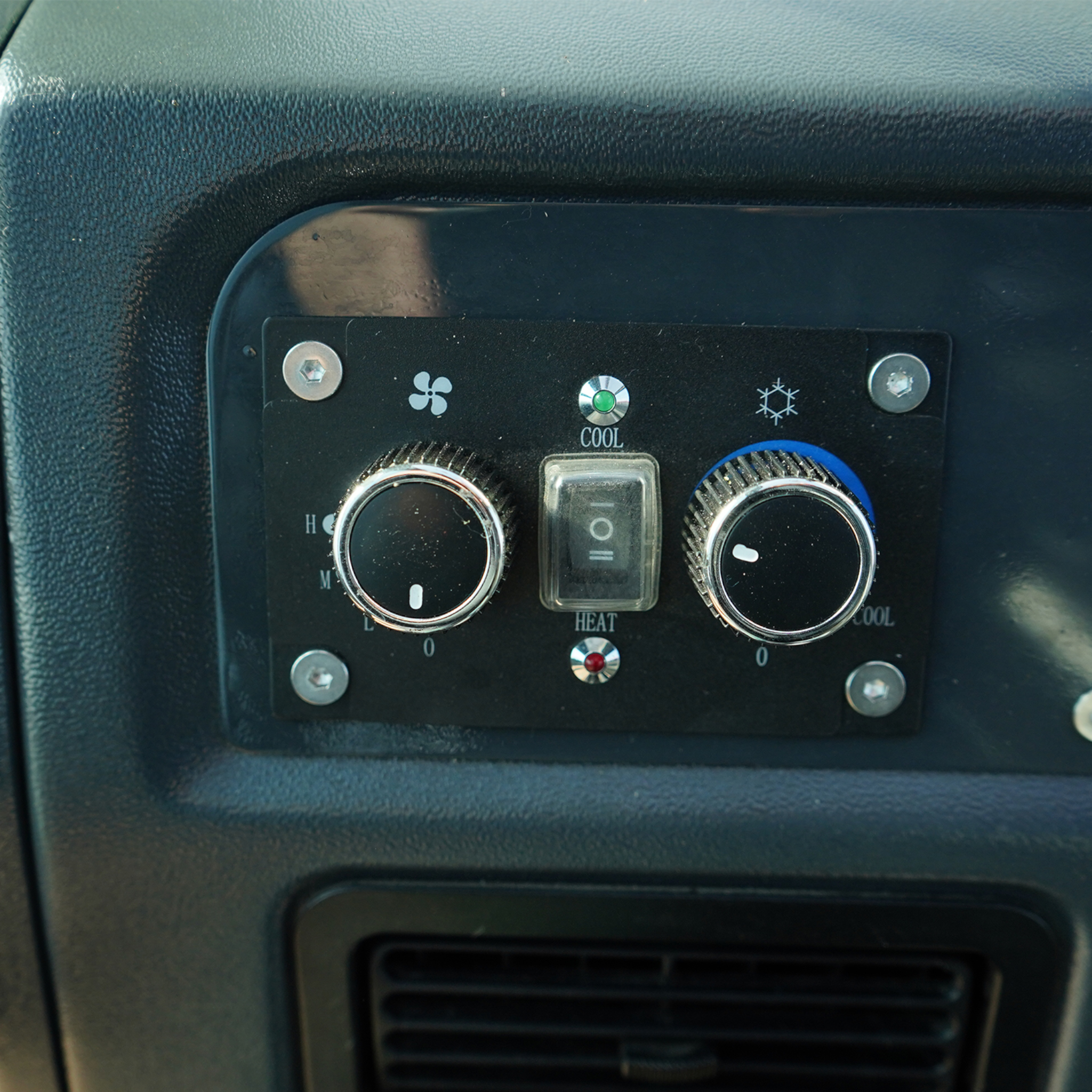 Close-up of a car dashboard HVAC panel with vents, dials, and metallic screws.