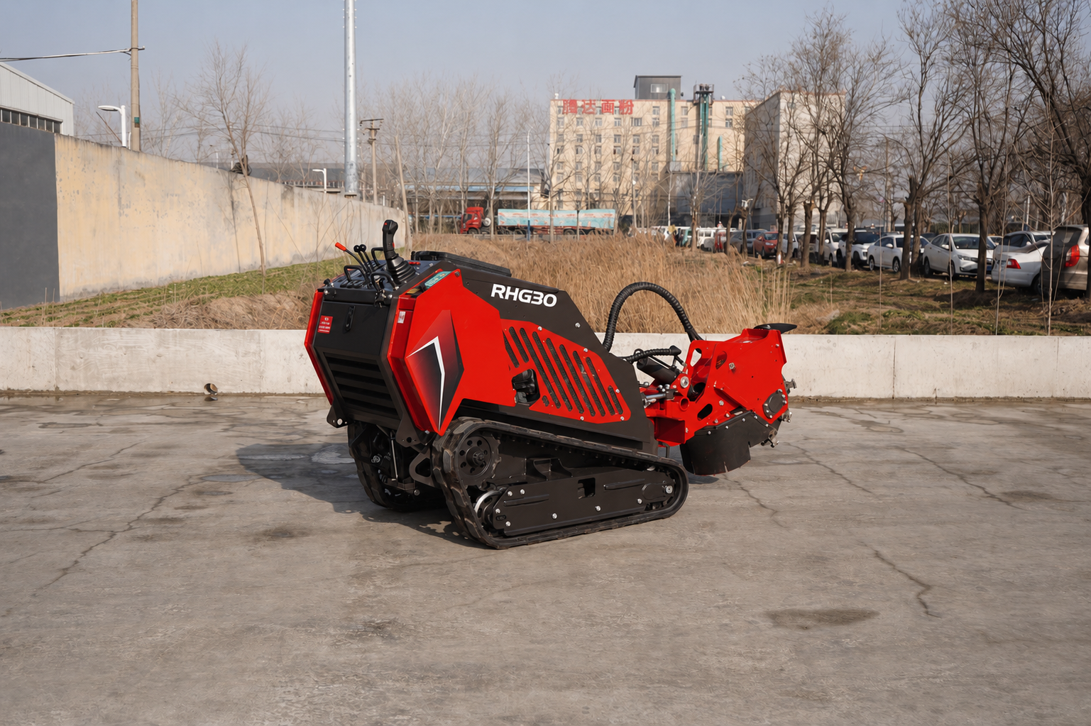 Red and black RHG30 tracked construction machine on a concrete lot with buildings and parked cars in the background.