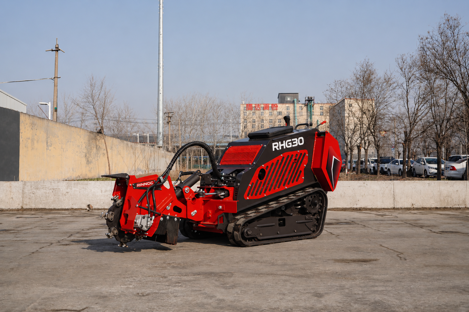 Red tracked road milling machine with RHG30 label parked on a concrete lot, industrial backdrop of trees and buildings behind it.