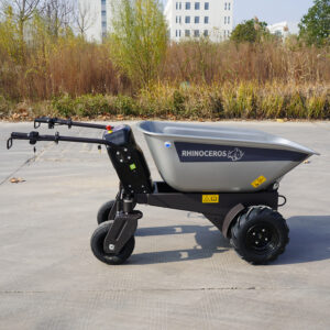 Motorized wheelbarrow with a gray cargo tub labeled RHINOCEROS, parked on concrete with bushes in the background.