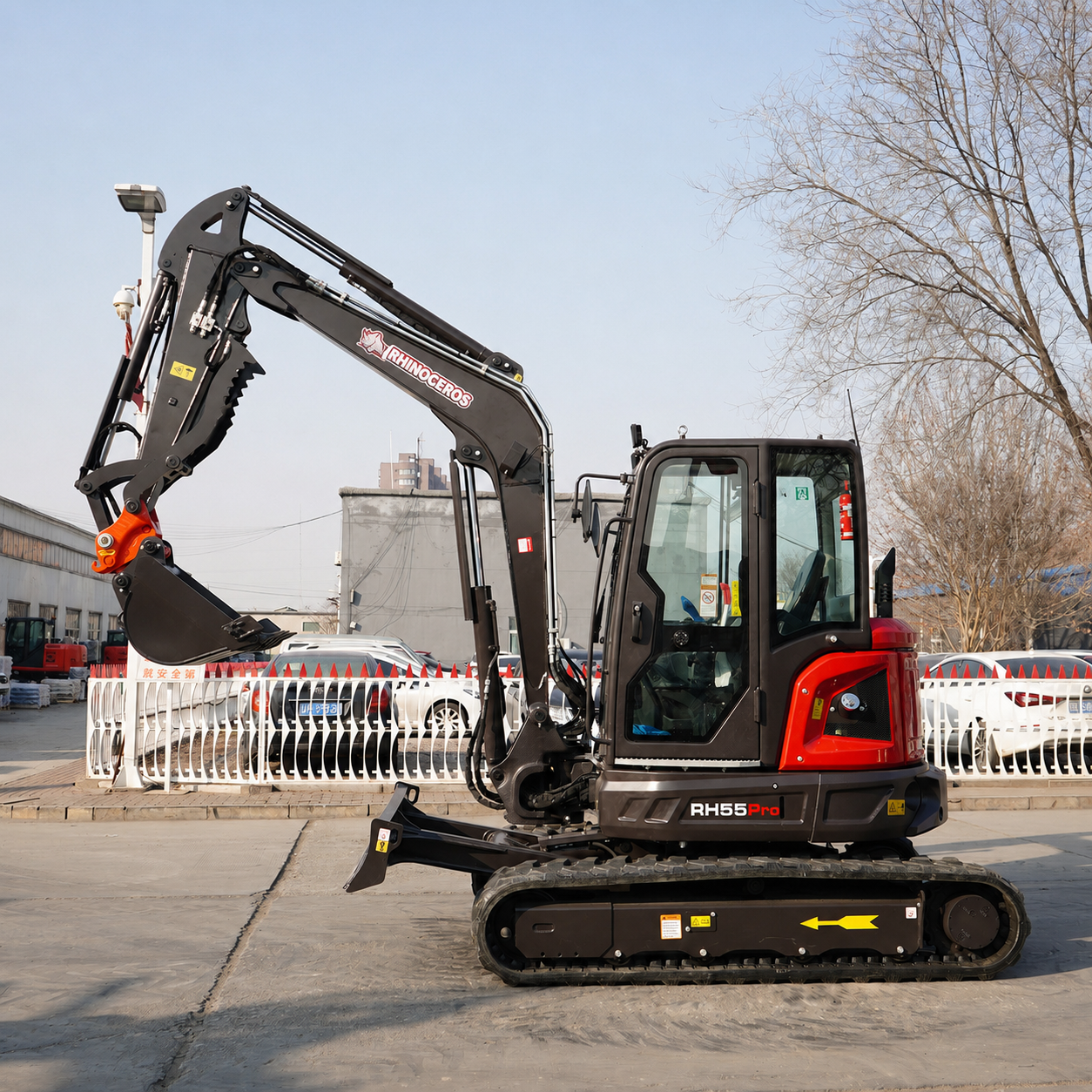 Compact mini excavator on tracks with its hydraulic arm raised, RH5 Pro, in a construction yard.