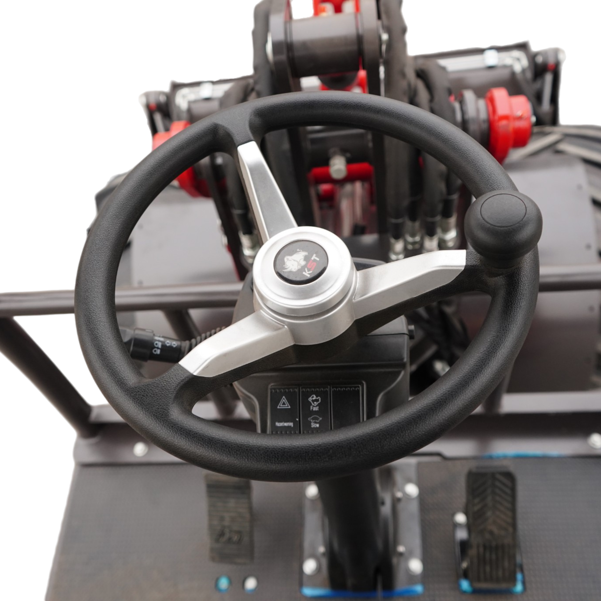 Close-up of a steering wheel in a heavy machinery cockpit with red control levers behind it and visible pedals behind the wheel.