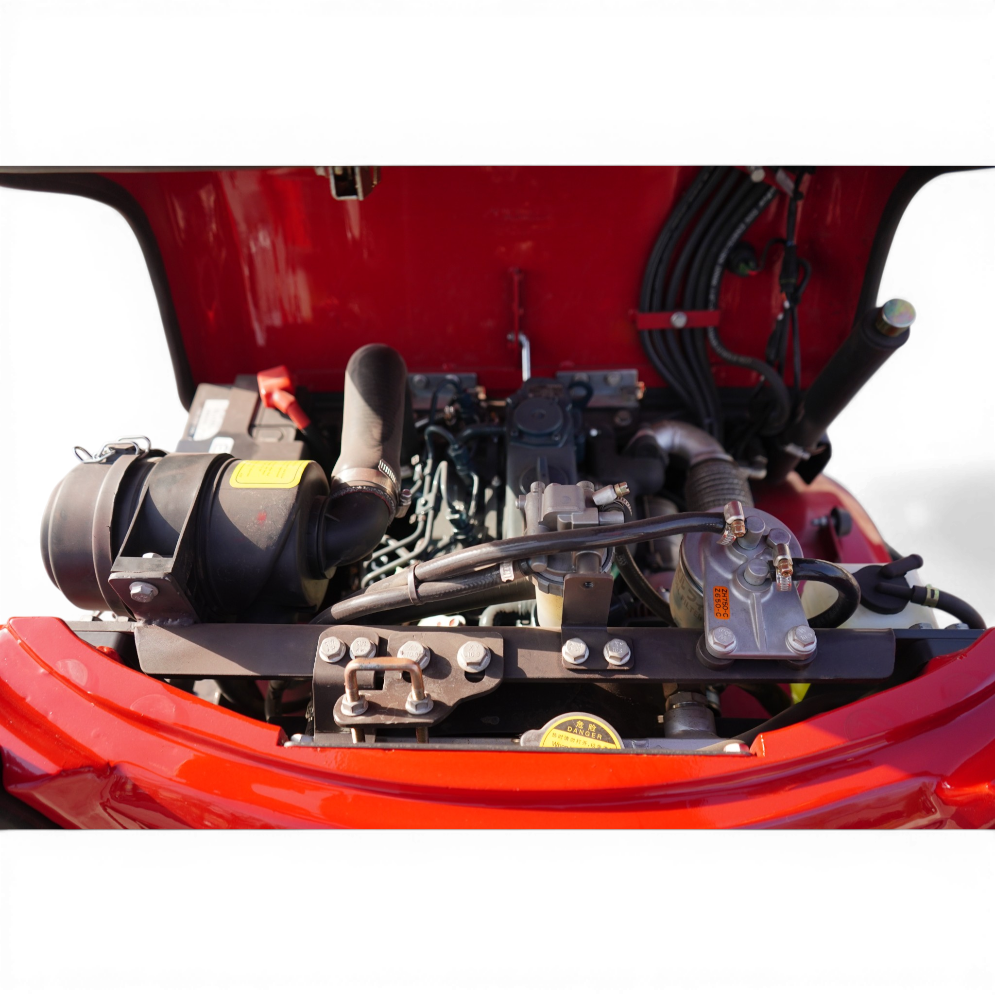 Close-up of a red vehicle's engine bay with hoses, wiring, and metal components visible beneath the open hood.